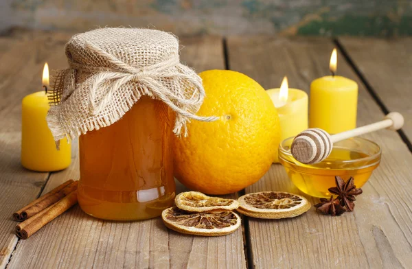 Банка меда, апельсины и свечи на деревянном столе — стоковое фото