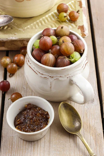 Jug of gooseberry fruits and bowl of gooseberry jam — Stock Photo, Image