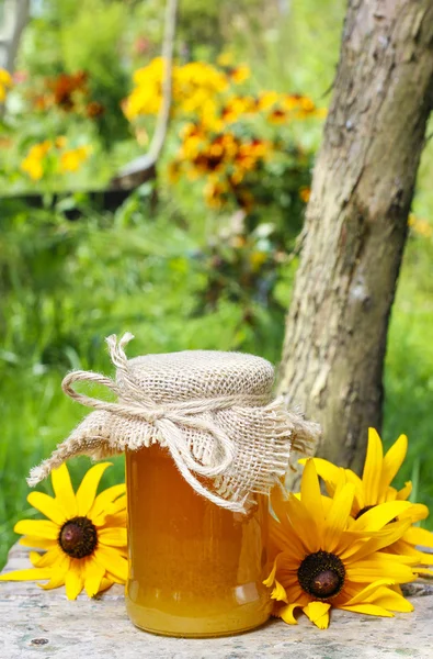Jar of honey and beautiful sunflowers in the garden — Stock Photo, Image