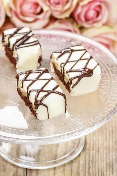 Chocolate and marzipan cakes on glass cake stand. — Stock Photo, Image