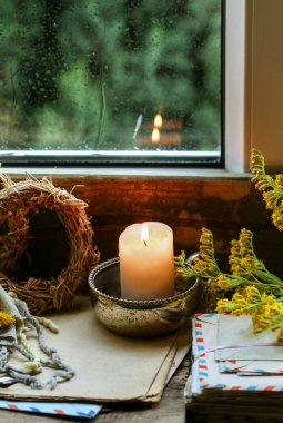 Pencerenin yanında bir mum ve etrafında sonbahar bitkileri. Ev dekoru