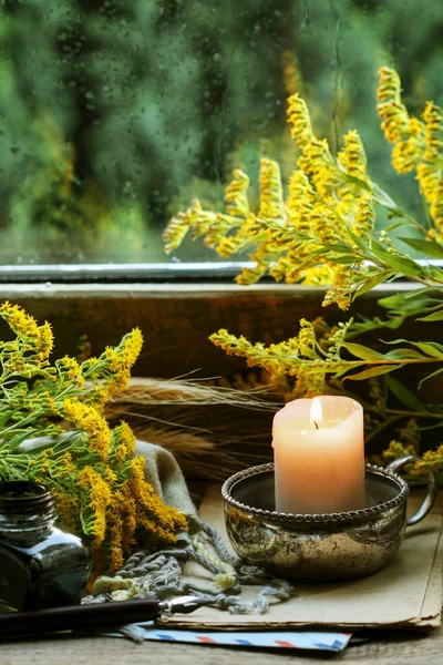 A candle by the window and autumn plants around it. Home decor