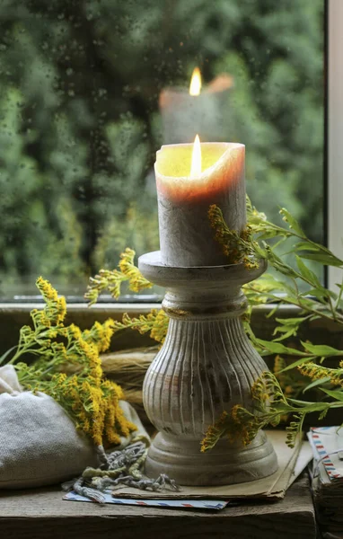 A candle by the window and autumn plants around it. Home decor