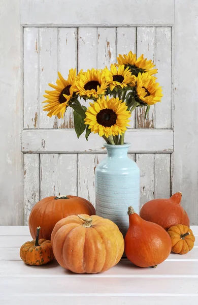 Bouquet of sunflowers in a ceramic vase and orange pumpkins around it. Autumn decor