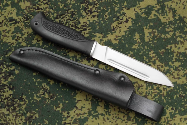 Vojenský nůž, která je rovnoběžná s černou koženou pochvou na maskování pozadí — Stock fotografie