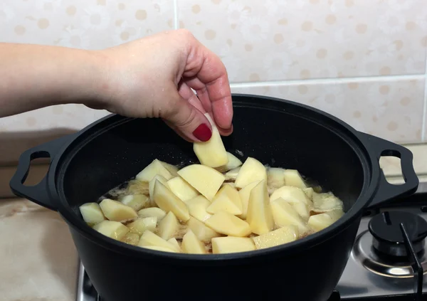 Woman's hand put a potato dice into the black metal saucepan — Stock Photo, Image