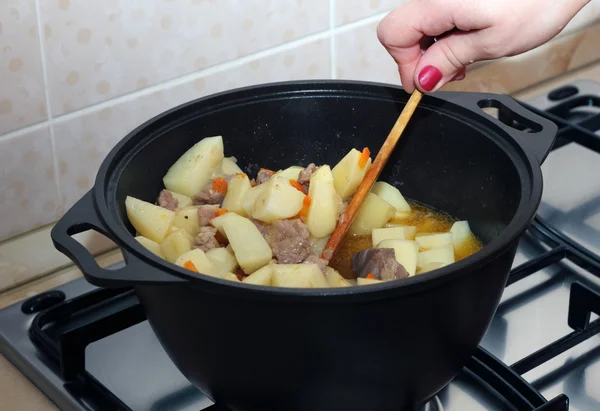 Woman's hand stiring ragout in the black metal pot — Stock Photo, Image