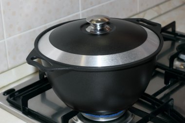 Black metal pot covered with a lid on the gas stove clipart
