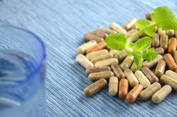 Herbal capsules and a glass of water — Stock Photo, Image