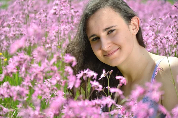 Menina morena atraente bonita sentada no prado lindo cheio de flores selvagens — Fotografia de Stock