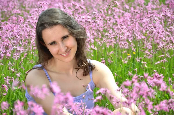 Menina morena atraente bonita sentada no prado lindo cheio de flores selvagens — Fotografia de Stock