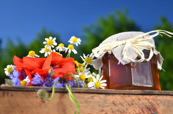 Frasco cheio de deliciosos mel fresco e flores silvestres em apiário contra o céu azul — Fotografia de Stock