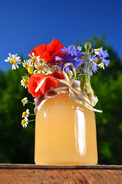 Jar full of delicious fresh honey and wild flowers in apiary against blue sky — Stock Photo, Image