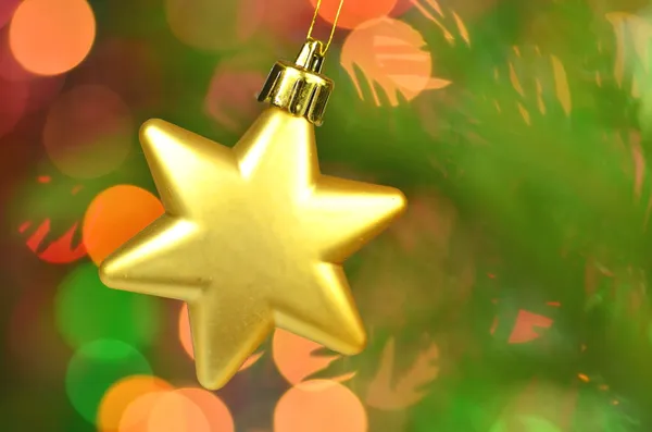Christmas decoration, golden Christmas star ball hanging on spruce twig against bokeh background — Stock Photo, Image