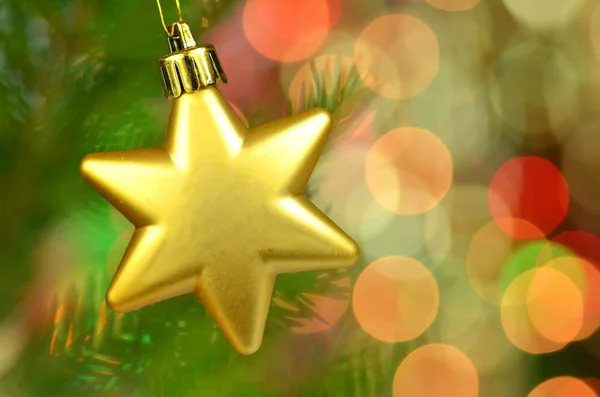 Christmas decoration, golden Christmas star ball hanging on spruce twig against bokeh background — Stock Photo, Image