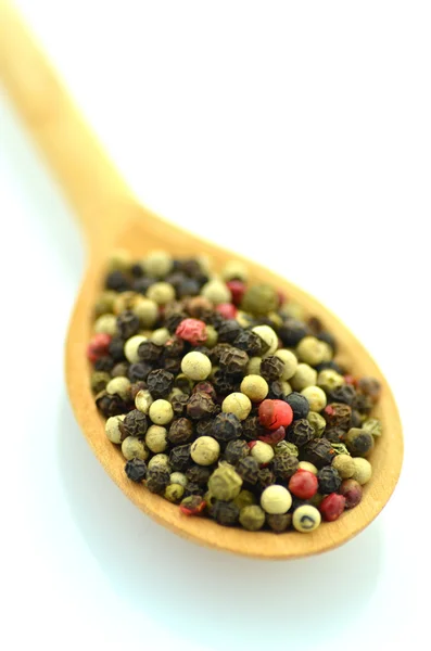 Closeup of colored pepper on a wooden spoon isolated on white background — Stock Photo, Image