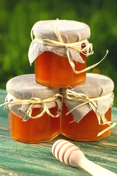 Wooden honey dipper and jars full of delicious fresh honey in apiary — Stock Photo, Image