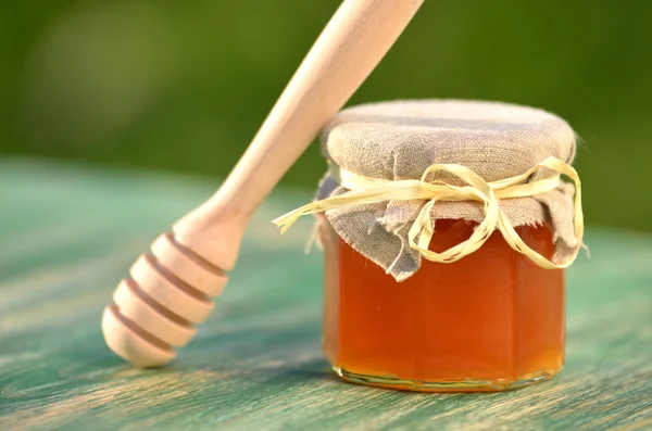 Mergulhador de mel de madeira e frasco cheio de mel fresco delicioso em apiário — Fotografia de Stock