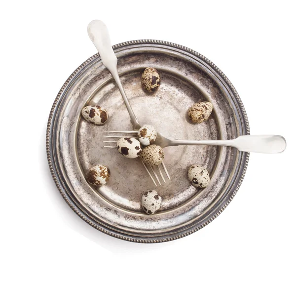 Clock made of quail eggs on silver plate with forks, isolated on white background — Stock Photo, Image