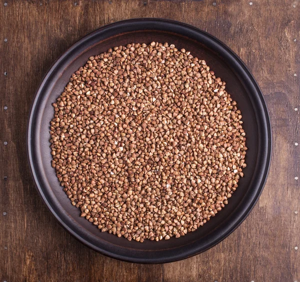 Organic buckwheat groats in plate on dark wood background — Stock Photo, Image