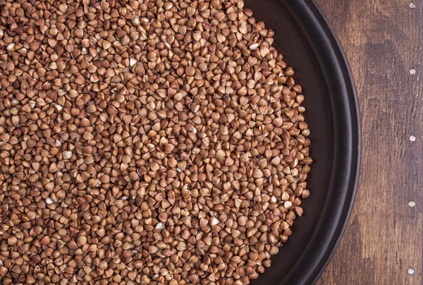 Organic buckwheat groats in plate on dark wood background — Stock Photo, Image