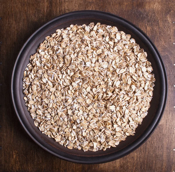 Piatto con farina d'avena cruda sul tavolo di legno . — Foto Stock