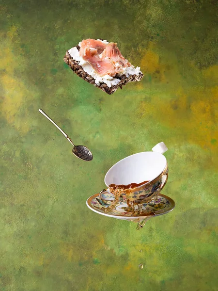 緑の背景に熱いお茶と魚のサンドイッチでカップを飛んでいます。浮揚. — ストック写真