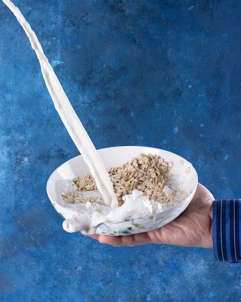 Płatki owsiane z rozbryzgami mleka na białej misce na niebieskim tle — Zdjęcie stockowe