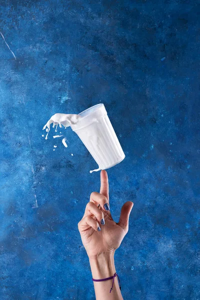 手で青の背景のガラスの上にミルクが飛び散った — ストック写真