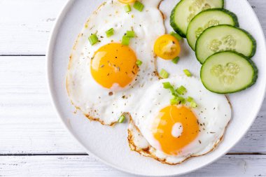 Beyaz ahşap arka planda beyaz bir tabakta sahanda yumurta sebzesi..