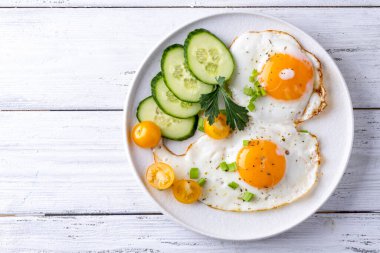 Beyaz ahşap arka planda beyaz bir tabakta sahanda yumurta sebzesi..
