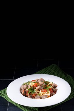 Domates soslu makarna, beyaz tabakta et ve siyah seramik arka plan..