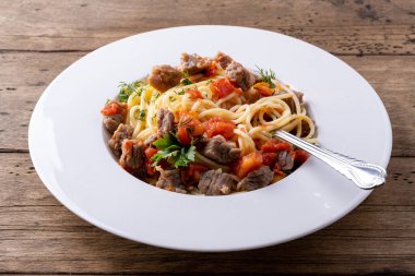 domates soslu makarna ve beyaz tabakta et ve ahşap zemin.