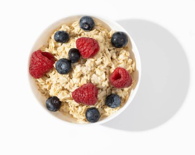 Beyaz masadaki beyaz kasede ahududu ve yaban mersini ile yulaf ezmesi. Üst görünüm