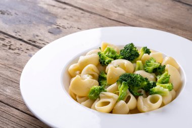 Beyaz tabakta brokolili makarna ve tahta masa..