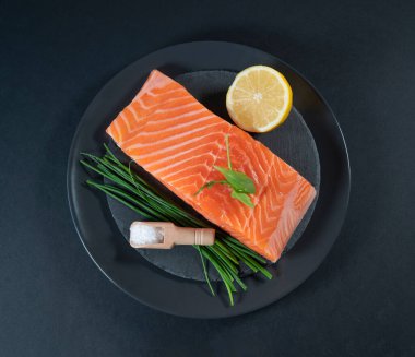 Taze çiğ somon balığı filetosu. Pişirme malzemeleri, otlar ve limon. Siyah arka planda.