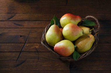 Eski ahşap bir masanın üzerindeki sepetin içinde olgun armutlar. Metnin için fotokopi alanı da var. Üst Manzara. Alçak tuş.
