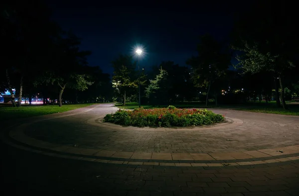 The teiled road in the night park with lanterns in autumn. Benches in the park during the autumn season at night. Illumination of a park road with lanterns at night. Flower bed. Park Kyoto