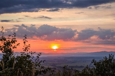 Dağlarda şafak vakti. Güneş dağların ardından doğar. Güzel yeşil tepeler ve yeşil vadi. Küçük uyuyan kasaba. Renkli bir gökyüzü, kırmızı bulutlar. Sisin içindeki dağlar. Karpatlar, Ukrayna,
