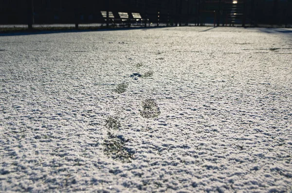 足球场上有人造绿草 覆盖着一层薄薄的雪 鞋底也有痕迹 足球场上的绿草在雪下看得见 业余足球场 — 图库照片