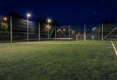 An amateur soccer field illuminated at night. A small football field lit by lanterns in the evening. Green football field illuminated at night. Soccer field in night with spotlight