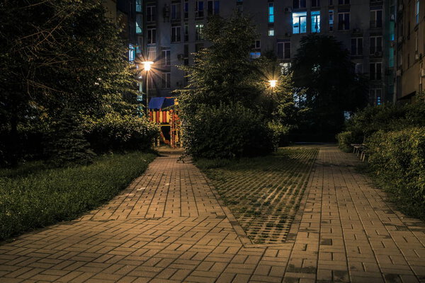 Night park paths and colored houses at summer night. Night paths, benches and lanterns in a beautiful residential complex. Night summer park with lanterns and benches. Kyiv. Ukraine