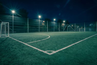 An amateur soccer field illuminated at night. A small football field lit by lanterns in the evening. Green football field illuminated at night. Soccer field in night with spotlight