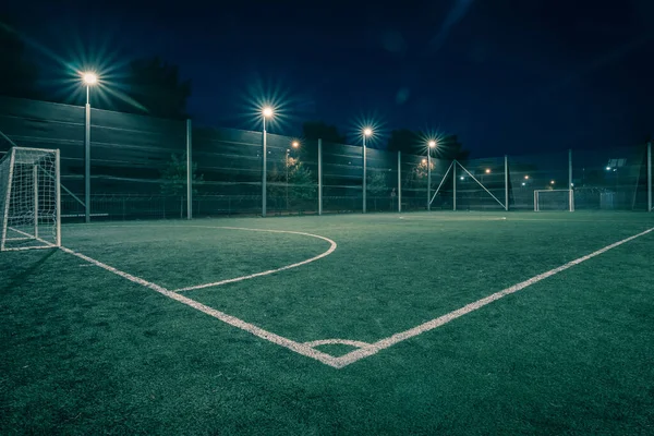 An amateur soccer field illuminated at night. A small football field lit by lanterns in the evening. Green football field illuminated at night. Soccer field in night with spotlight