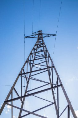 High voltage, power transmission line on the mountain range on a blue sky background. Overhead power line in the mountains. Metal poles of power lines in the mountains