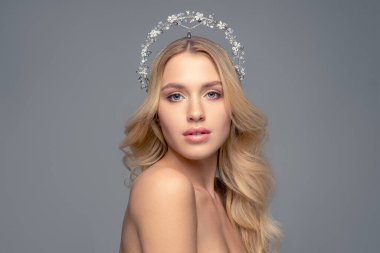 Saçları gri arkaplanda, güzel bir sarışının portresi. Kafasında küçük taşlarla süslenmiş.