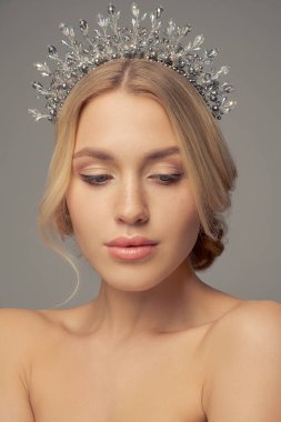 Saçları gri arkaplanda, güzel bir sarışının portresi. Kafasında küçük taşlarla süslenmiş.