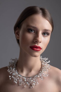 Siyah saçlı, kırmızı rujlu ve boynunda taş süsü olan bir kızın profili..