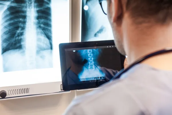 Doctor with tablet examing x-ray pictures — Stock Photo, Image