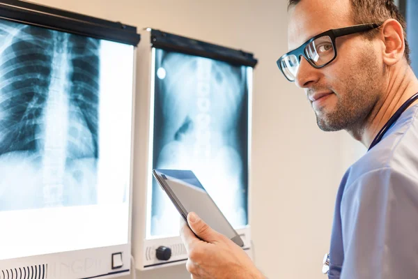 Doctor with tablet examing x-ray pictures — Stock Photo, Image